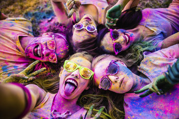 Group of friends lying in a circle covered in colorful powder, laughing and smiling together