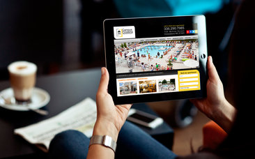Hands hold a tablet displaying a property website with a pool photo and contact phone number