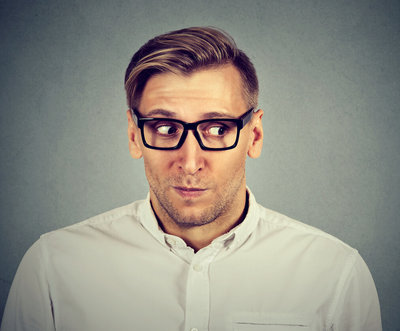 Man in glasses and white shirt glances sideways with a nervous expression against a gray background