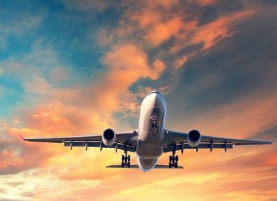 Commercial airplane with landing gear extended ascending into a sunset sky with orange and blue clouds