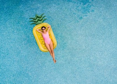 Woman in a pink swimsuit relaxes on a pineapple-shaped pool float in a blue pool