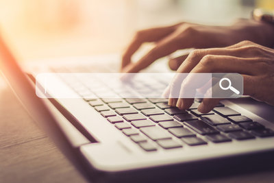 Hands typing on a laptop keyboard with a search bar graphic overlaid on the screen