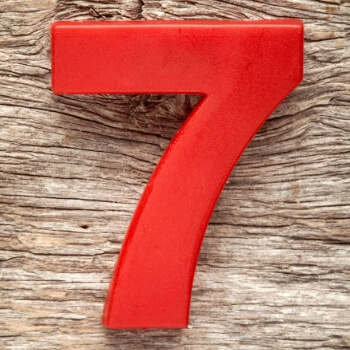 Red numeral seven with a glossy finish rests on a weathered wooden surface