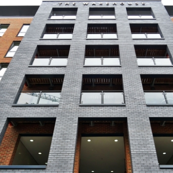 Gray brick apartment building facade with large windows and illuminated ground-floor lobby spaces
