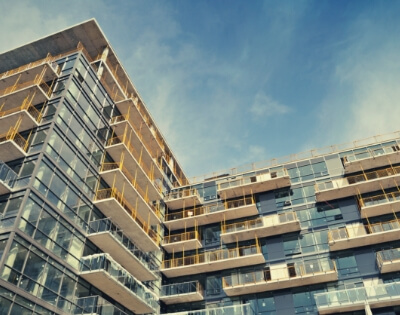 Modern multifamily buildings with glass balconies and railings viewed from below against a blue sky