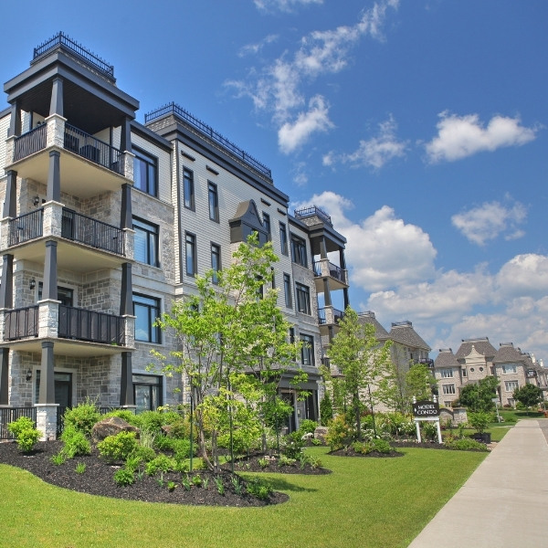 Multi-story stone condominium building with balconies and landscaped lawn under a blue sky