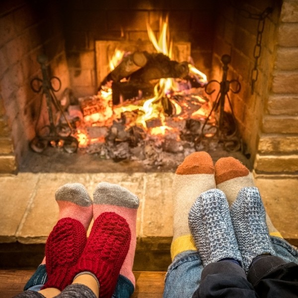 Three pairs of feet in cozy socks warm up near a crackling fireplace