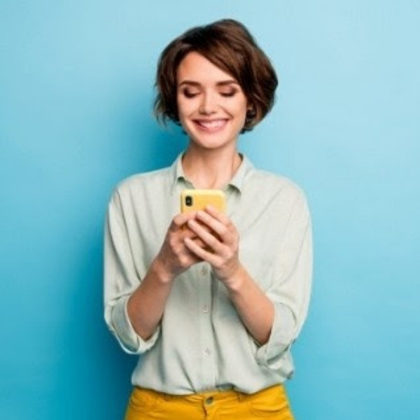 Smiling woman with short brown hair texting on a yellow smartphone against a blue background