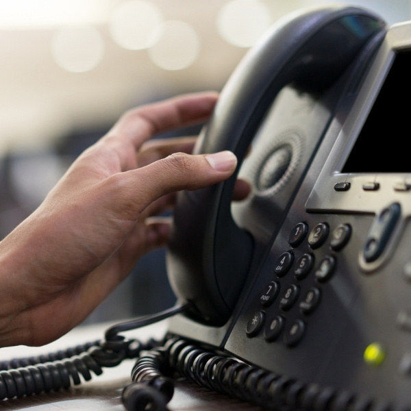 Hand reaching to pick up a desk phone handset on an office telephone