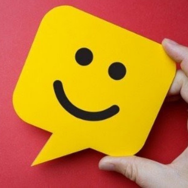 A hand holds a yellow speech bubble shaped card with a smiling face against a red background