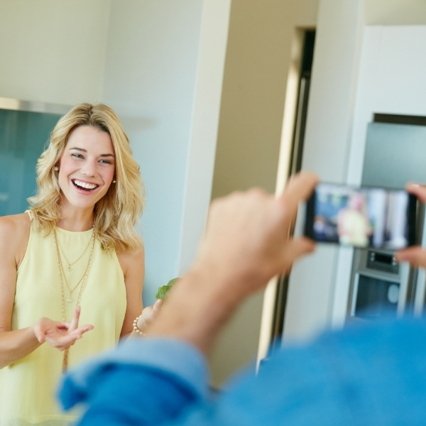 A smiling woman is filmed on a smartphone by someone in the foreground during a video shoot