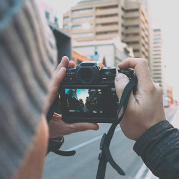 Person holds a mirrorless camera over their shoulder, framing a city street on the display screen