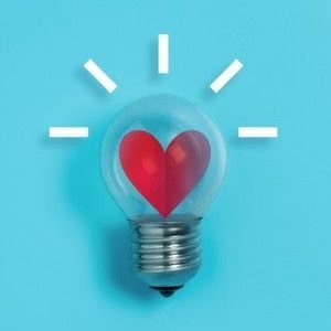 A light bulb with a red heart inside sits against a blue background surrounded by small rectangular light rays.